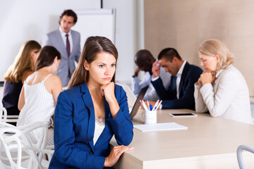 Young woman sitting in meeting room looking upset because of angry boss scolding her coworkers
