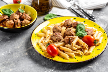 penne pasta with meatballs and tomato sauce, on a yellow plate and a gray background