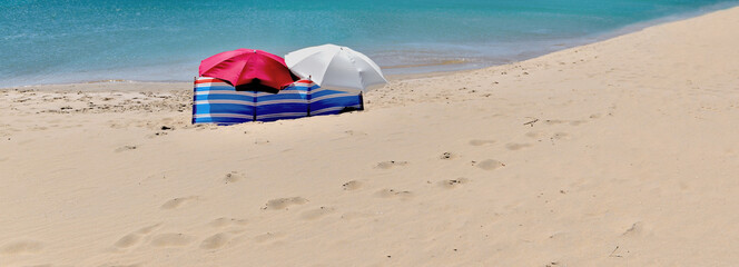 beach umbrellas windscreen sheltering people not visible alone on a beach with fine sand and turquoise sea