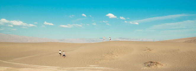 Fototapeta na wymiar Desert hiking. Tourists hiking among sand dunes. Mesquite Sand Dunes in Death Valley National Park, California