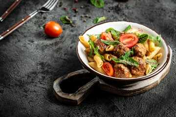 Italian pasta. penne pasta with meatballs in tomato sauce in a white craft bowl on a grey stone background. banner, menu recipe place for text, top view