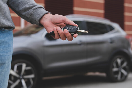 Man in front of the new car and holding keys. Salesman is carrying the car keys delivered to the customer at the showroom with a low interest offer.  Rent, credit, insurance, car purchase. Copy space