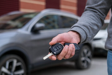 Man in front of the new car and holding keys. Salesman is carrying the car keys delivered to the customer at the showroom with a low interest offer.  Rent, credit, insurance, car purchase. Copy space - obrazy, fototapety, plakaty