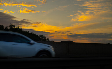 Fototapeta na wymiar Fast moving car in expressway early in the morning against bright yellowish clouds.