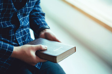 man sitting while holing bible or book over concrete wall with window light