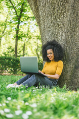 Beautiful and happy afro woman typing on a laptop in a garden.