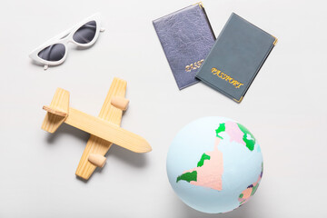 Globe with wooden airplane, sunglasses and passports on light background