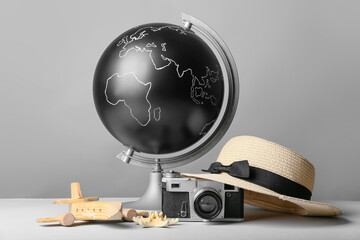 Globe with wooden airplane, photo camera and hat on grey background