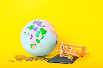 Globe with wooden airplane, coins and passport on color background