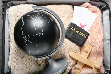 Globe with wooden airplane, passport and tickets on packed suitcase