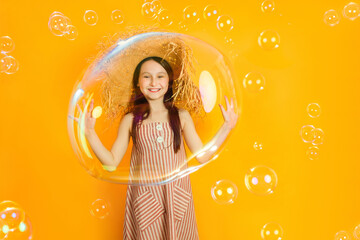 Little happy girl playing with huge soap bubbles on a colored yellow background. The child have fun...