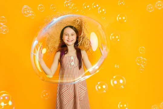 Little happy girl playing with huge soap bubbles on a colored yellow background. The child have fun inside the bubbles.
