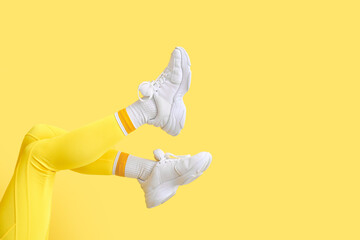 Legs of stylish young woman in leggings on yellow background - obrazy, fototapety, plakaty
