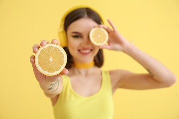 Stylish young woman with cut lemon on yellow background