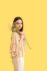 Stylish young woman with flowers on yellow background