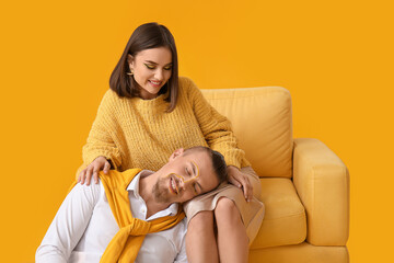 Stylish young couple with armchair on yellow background