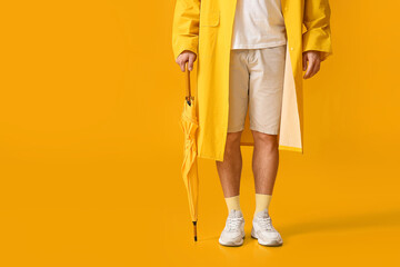 Stylish young man with umbrella on yellow background