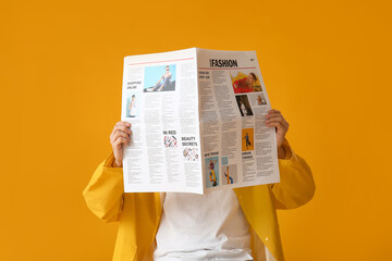 Stylish young man with newspaper on yellow background