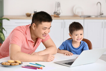 Father and his little son with laptop in kitchen