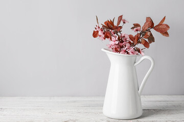 Vase with beautiful blossoming branches on table against light background