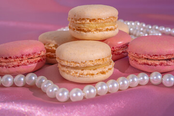 Pink and beige macarons on pink silk background with pearl necklace. French Pastel Macaroons. Selective focus