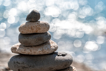 Tower of stones. Balanced pebble pyramid on the beach on a sunny day. Blue sea on the background. Selective focus, bokeh. Zen stones on the sea beach, meditation, spa, harmony, tranquility, balance
