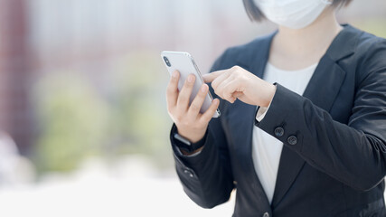 屋外でスマートフォンを操作するマスク姿のビジネスウーマン