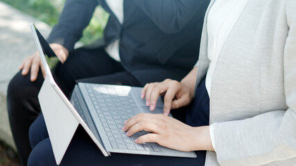 屋外でノートパソコンを見ながら話し合う二人のマスク姿のビジネスウーマン