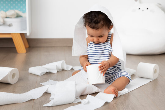 Cute baby sitting on floor making mess with toilet paper