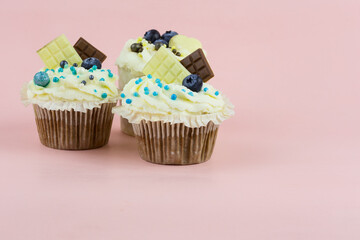 Small holiday cupcakes with berries and decor on a pink background. Fresh and beautiful cakes with berries
