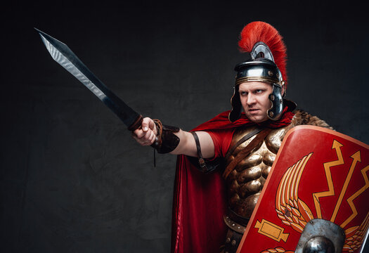 Angry roman soldier points sword against dark background