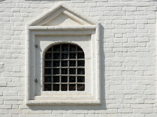 Fototapeta na wymiar Figured window with iron grid in ancient white brick wall. Medieval historical background.