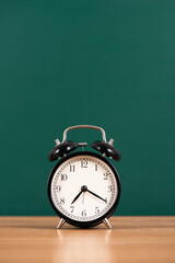 Alarm clock over blackboard  on table background,back to school concept