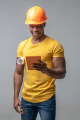 Dark-skinned construction worker in helmet with tablet