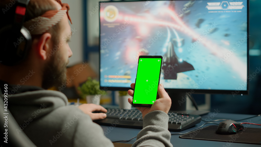 Poster concentrate gamer holding phone with green screen mock up chorma key display while playing games on 