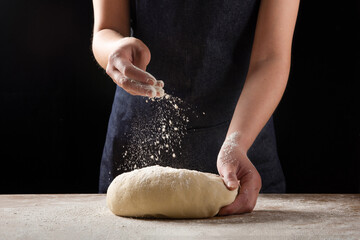 Cook hands kneading dough, sprinkling piece of dough with white wheat flour.