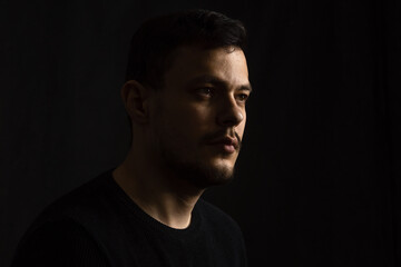 The face of a young, dark-haired man against a dark background. The emotion of sadness, tragic memories.