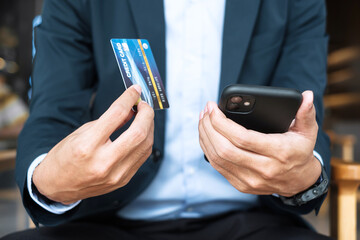 Businessman in suit holding credit card and using touchscreen smartphone for online shopping while making orders in the cafe or office .business, technology, ecommerce and online payment concept