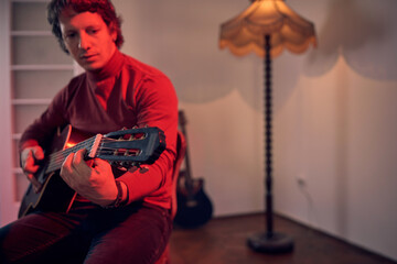 Male musician playing acoustic guitar on the amplifier in retro vintage room.
