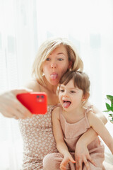 Cute little girl and her young mother fooling around, taking selfies