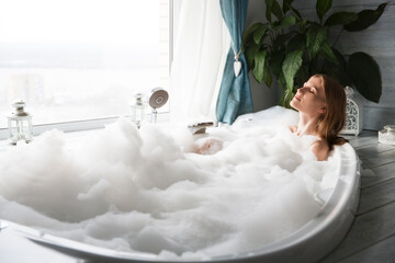 a young woman relaxes in the bathroom with foam at home