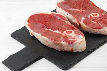 Raw lamb steak on board on white wooden table