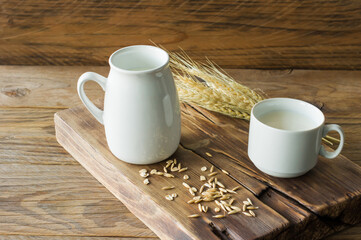 Oat milk in glass pitcher and oatmeal in a cup on a wooden table.