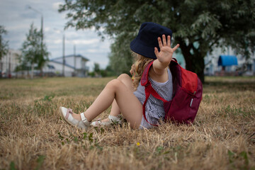 the girl sits on the grass and covers herself from the camera with her hand