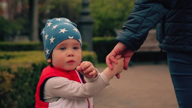 Boy 2 years old, walking with mother in the park. Bright red jacket and blue cap in the stars. Mom and sun