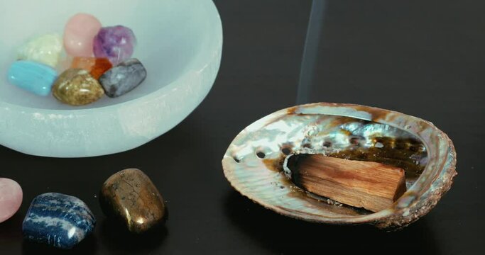 Palo santo burning on an abalone shell next to a bowl of crystals