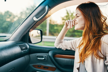 Fototapeta na wymiar happy woman with red hair in front seat of car touching face with hands cropped view