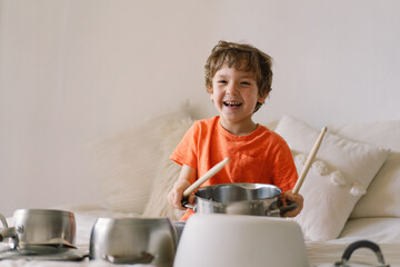 Cute young boy using wooden sticks to bang saucepans that are set up like a drumset.