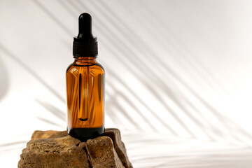 Dark glass cosmetic bottles with a dropper on a beige background with stones and tropical leaves. Natural cosmetics concept, natural essential oil and skin care products
