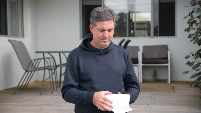 Mature adult man (male age 40-50) reading a bad posted letter in home front yard.